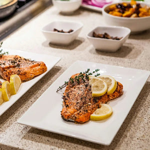 Plated salmon with lemon slices on a countertop with additional plates and bowls in the background.