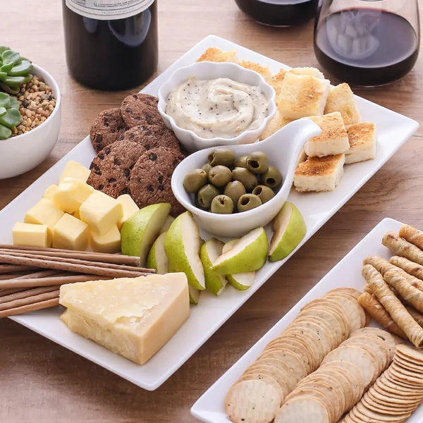 rectangular platter of assorted cheeses, crackers, olives, and bread on a wooden table with wine glasses.
