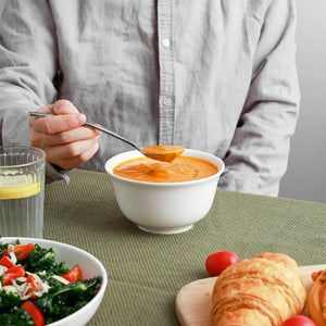 Person eating soup from a bowl with a side of salad and bread on a green tablecloth.