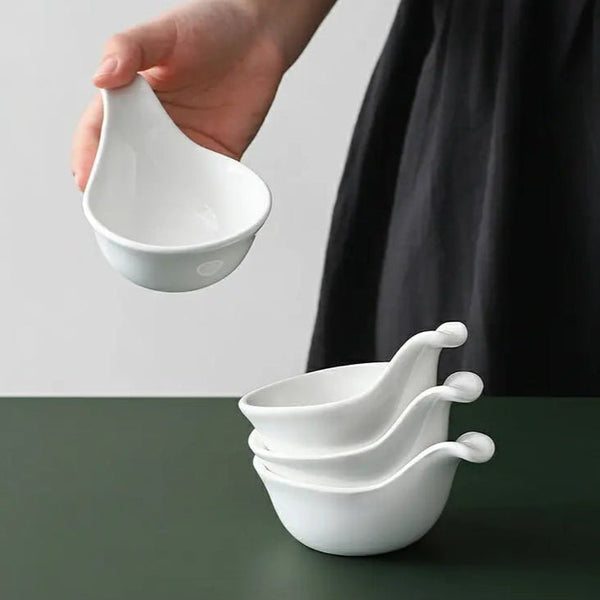 White ceramic ladles being held and stacked on a green surface with a white background