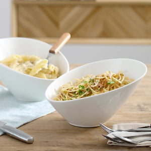 Two white bowls of pasta on a wooden table with a blurred background