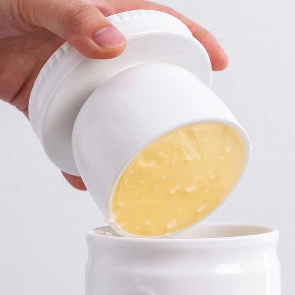 Hand pouring a yellow substance from a white container into another white container.