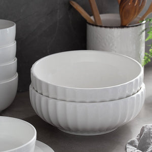 Stack of white ceramic bowls on a kitchen counter with utensils in the background.