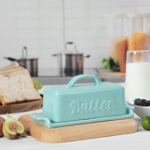 Turquoise butter dish on a kitchen counter with bread, figs, and milk.