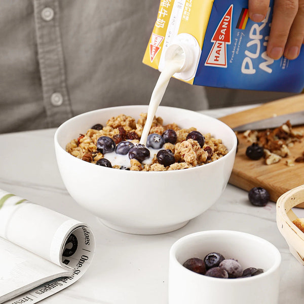 Person pouring milk from a Hansani container into a bowl of cereal with berries.