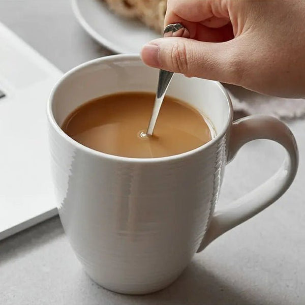 Person stirring a cup of coffee with a spoon on a light surface.