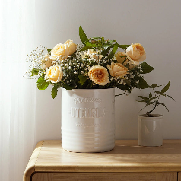 White vase with yellow roses on a wooden surface against a light background