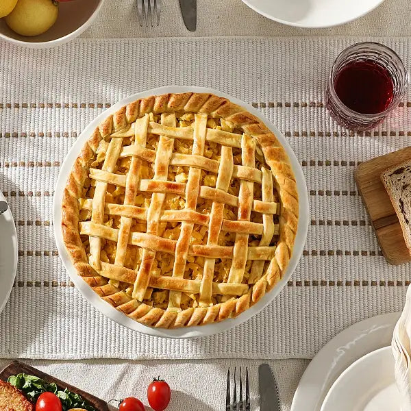 Lattice-topped pie with the pie plate on a table with a glass of red wine and bread.