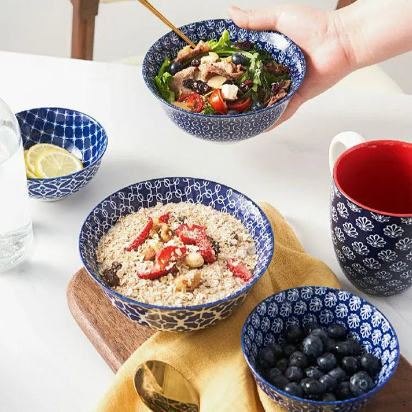 Bowl of salad with a hand holding it, surrounded by other bowls and a mug on a white surface.