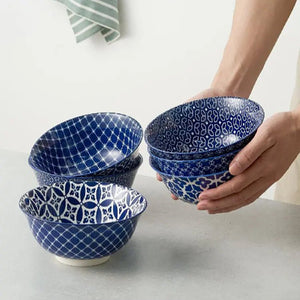 Set of blue patterned ceramic bowls on a light surface with a hand holding one bowl.