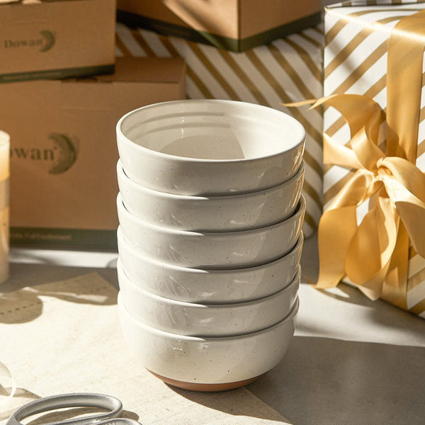 Stack of white ceramic bowls on a surface with gift boxes in the background