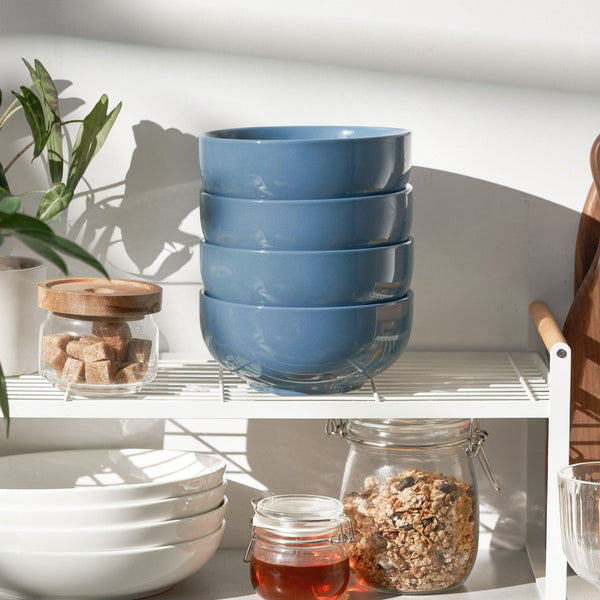 Stack of blue bowls on a kitchen shelf with jars and a plant.