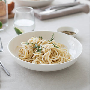 White bowl of spaghetti with herbs on a light gray surface