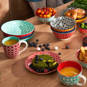 Colorful ceramic dishes and mugs on a wooden table with food.