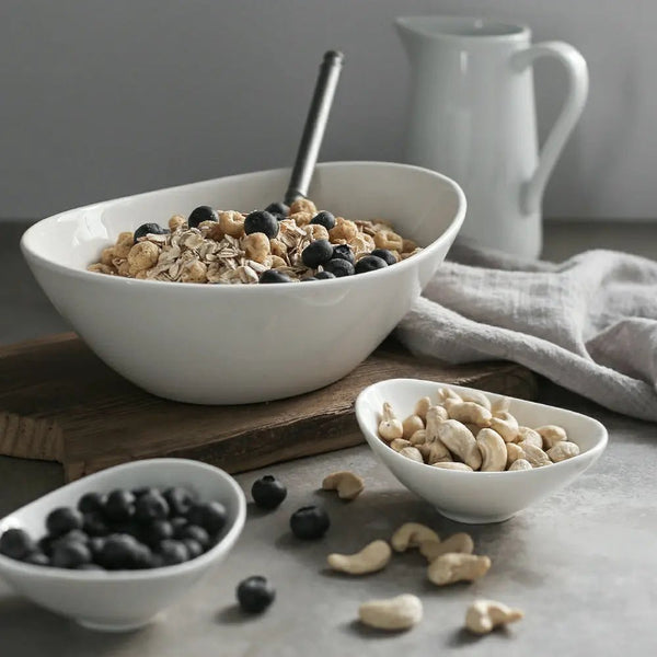 White bowl of granola with blueberries and a smaller bowl of nuts on a wooden surface.