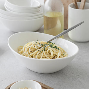 White bowl of spaghetti with a fork on a gray surface with kitchen items in the background