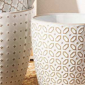 Three ceramic pots with geometric patterns on a textured surface