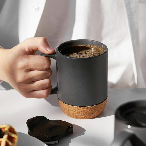 Person holding coffee mugs with cork bottom on a white surface