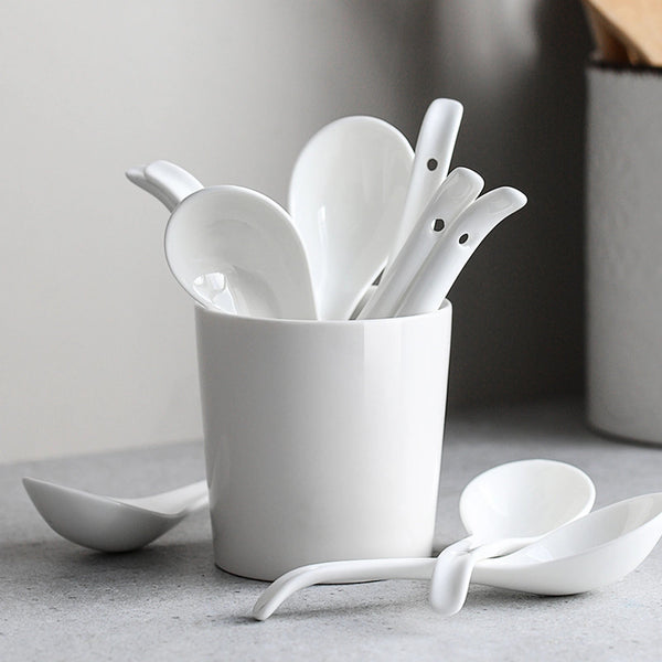 Set of white ceramic spoons in a cup on a gray surface