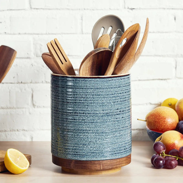Blue textured kitchen utensil holder with wooden utensils on a white brick wall background.