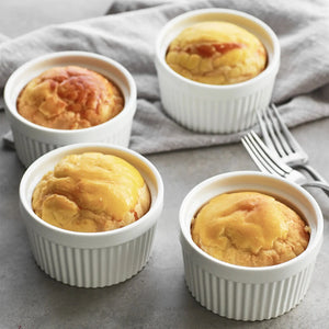 Four small baked goods in white ramekins on a gray surface with a fork.