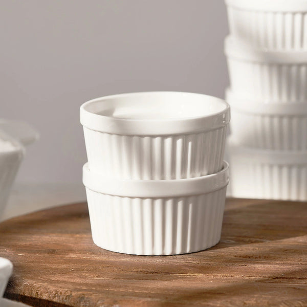 Two white ceramic ramekins stacked on a wooden surface with a neutral background