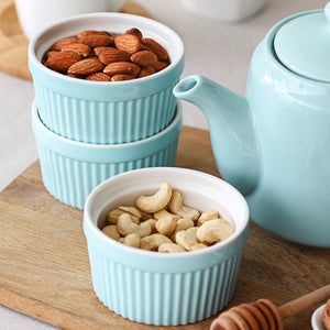 Teal ceramic bowls with nuts on a wooden surface next to a teapot.