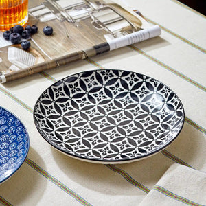 Ceramic plate with black geometric pattern on a table with a glass of tea and blueberries.