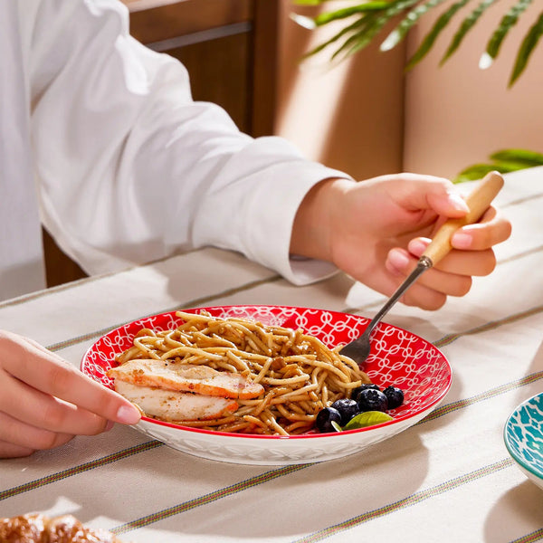Person eating spaghetti with a fork on a red plate at a table.