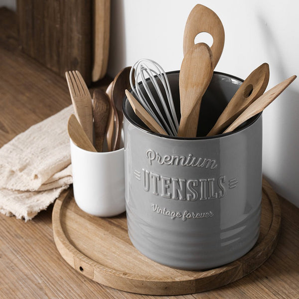 Gray utensil holder with wooden spoons and a whisk on a wooden surface.