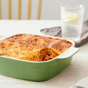 Baked dish in a green casserole dish on a table with a glass of water in the background.