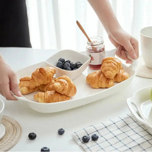 Person holding a plate of croissants and blueberries on a white table.